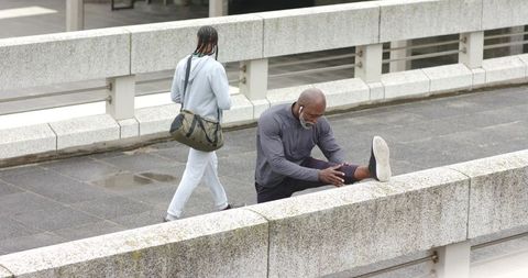 Man Stretching on Urban Overpass Rail While Passerby Walking in Light Drizzle