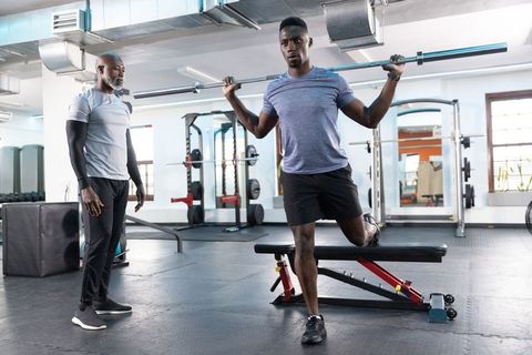 African American Trainer Coaching Athlete Performing Barbell Bulgarian Split Squat on Bench