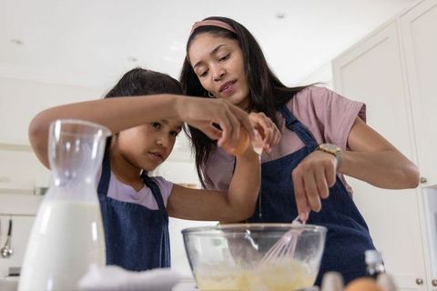African american mother and daughter baking together, whisking batter and bonding in home kitchen
