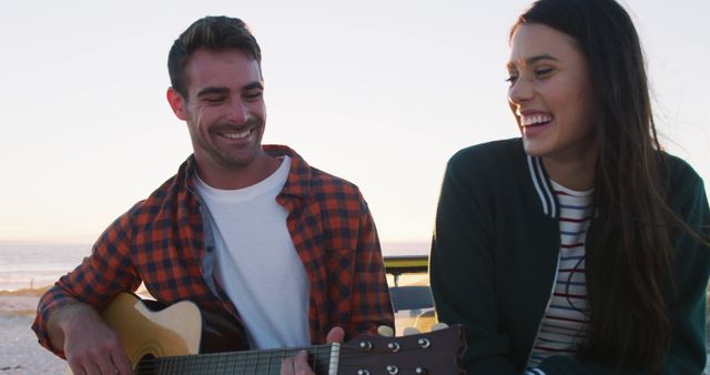 Happy caucasian couple sitting in beach buggy by the sea playing guitar. beach stop off on summer holiday road trip.