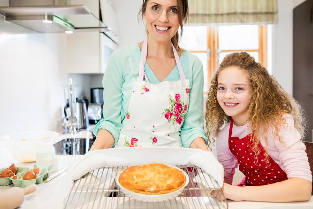 Portrait of mother and daughter holding pancake in cooling rack at kitchen