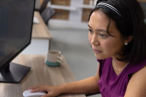 Focused asian woman utilizing computer in modern workspace