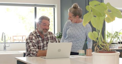 Mature couple laughing together over laptop in modern kitchen