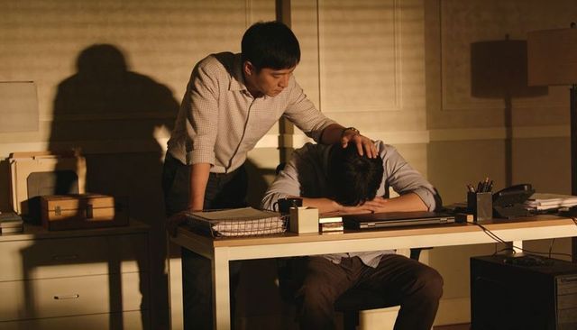 Colleague consoling stressed coworker at late-night office desk under warm lamplight