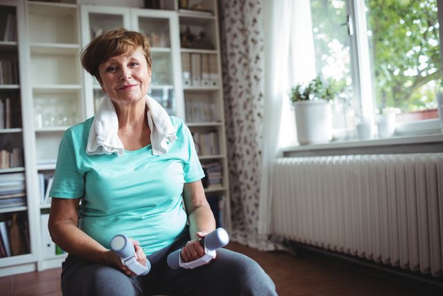 Portrait of senior woman sitting on exercise ball with dumbbells at home