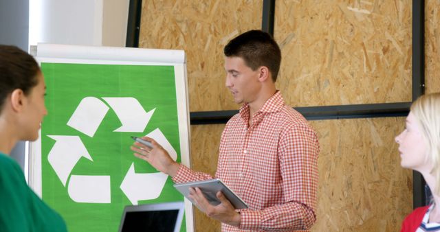 A young Caucasian businessman is presenting a recycling concept to colleagues, with copy space. His presentation includes a large recycle symbol, indicating a focus on sustainability and environmental responsibility.