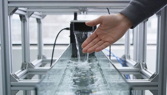 Technician guiding water flow in glass flume with pump and tubing on lab bench