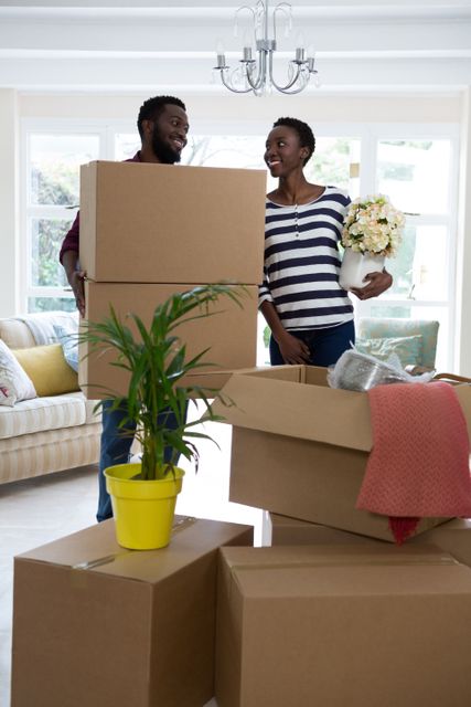 Happy couple carrying big cardboard box and vase at new home