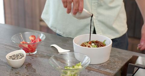Hands Pouring Sauce into Bowl of Grains in Minimalist Kitchen