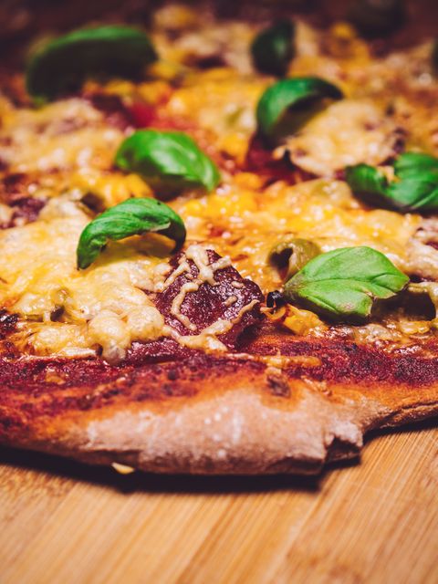 Close-up view of a cheesy homemade pepperoni pizza with fresh basil leaves on top. Ideal for food blogs, culinary websites, cookbooks, restaurant menus, and social media posts celebrating Italian cuisine and comfort food.