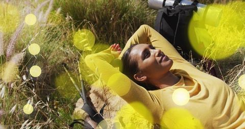 Woman Relaxing on Rock in Sunny Meadow with Camping Gear