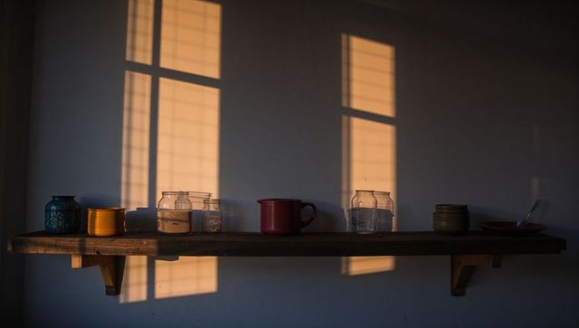 Sunlight casting grid window shadows on minimalist wooden shelf with jars and red mug