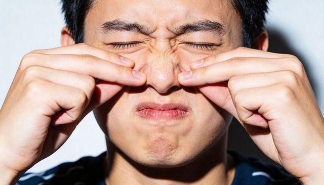 Teenage asian male pinching nose grimacing closeup conveying disgust and discomfort