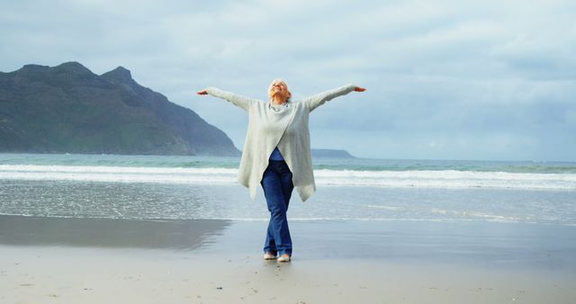 Senior woman standing with hands raised on beach during winter