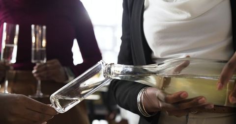 Diverse women pouring sparkling wine into flute at elegant reception, celebrating with bracelets