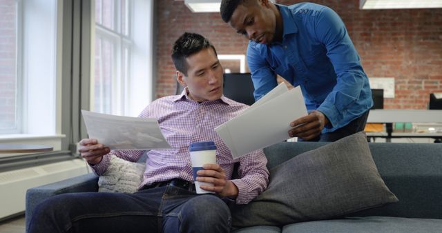 Asian man and African American man review documents in an office. They collaborate on a project, sharing insights and strategies.
