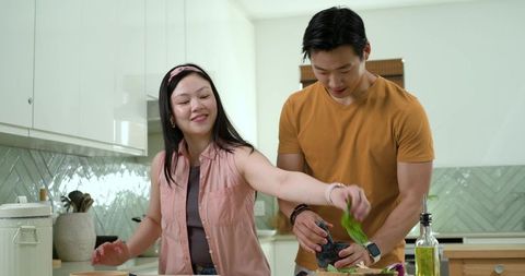 Asian couple preparing healthy meal together in kitchen sharing fresh herbs and teamwork