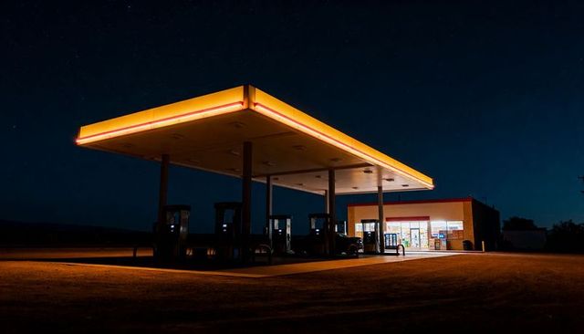 Orange-trim canopy lighting illuminating rural gas station forecourt under starry night