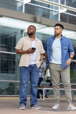 Two african american colleagues walking outside modern office canopy holding smartphone