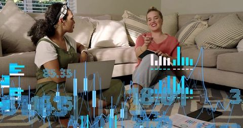 Women collaborating on living room floor using laptop and charts with digital data overlays