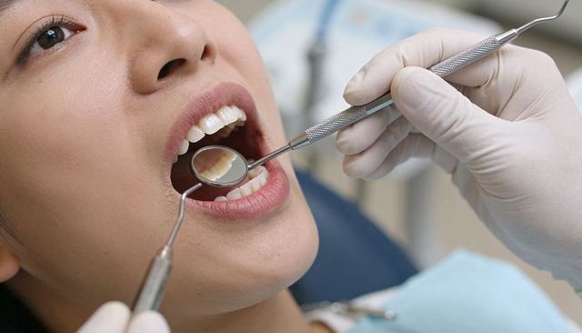 Asian woman receiving dental oral exam with mirror and probe in dental chair close-up