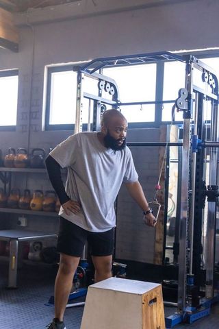 African american man training with cable machine near plyo box and kettlebells
