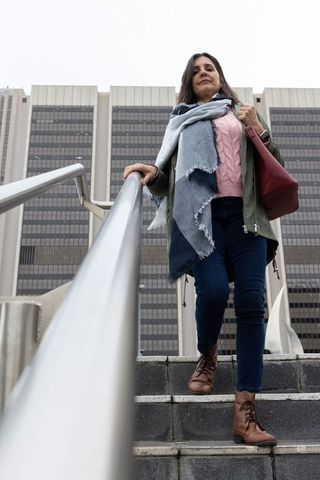 Confident commuter descending urban stairs wearing scarf and carrying leather tote