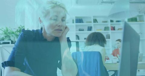 Female professional leaning at desk watching monitor in modern open-plan coworking office