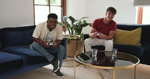 Black and White friends playing console games on navy velvet sofas in bright modern home