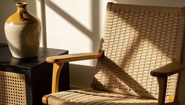 Woven cane armchair and ceramic jug bathed in warm soft sunlight casting textured shadows