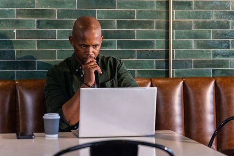 Remote professional working on laptop in cafe with coffee, smartphone and green tile wall