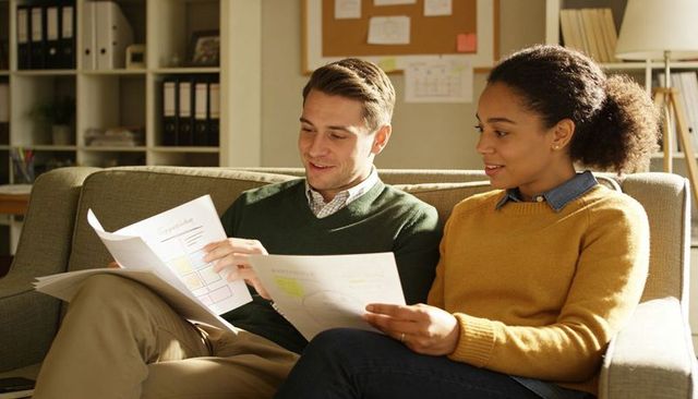 Colleagues collaborating over printed charts on sofa in modern office with warm lighting