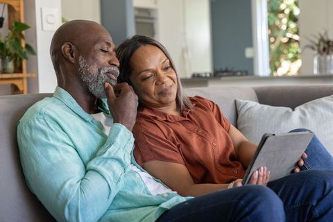 Senior couple relaxing on sofa and sharing tablet in cozy open-plan living space
