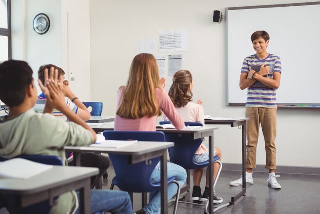 Schoolboy standing in front of classroom giving presentation to classmates. Students sitting at desks, listening and clapping. Ideal for educational content, school brochures, academic articles, and teaching resources.