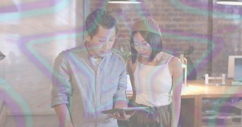 Young professionals collaborating over tablet in loft with neon star overlay, creative studio