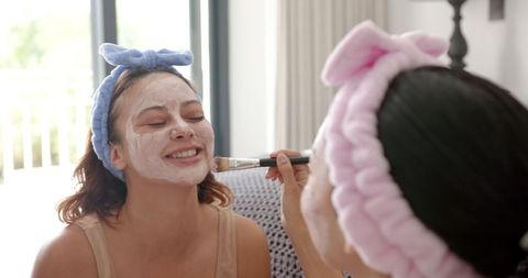 Two friends enjoying spa day with facial masks at home