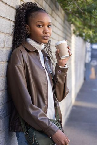 African american woman leaning brick wall holding coffee cup urban street style portrait