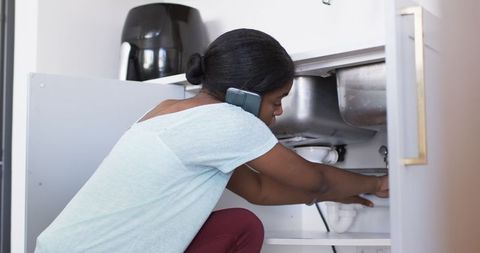 Focused woman fixing sink with phone communication