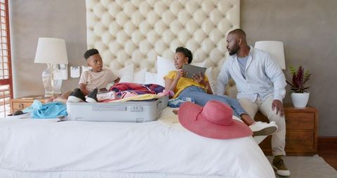 African American family packing for vacation on bed sharing tablet and open suitcase