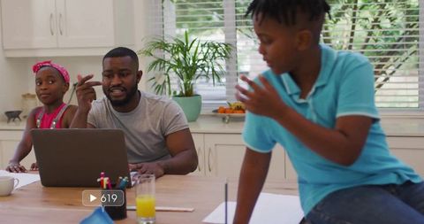 Working father balancing laptop work and supervising kids doing homework at kitchen table