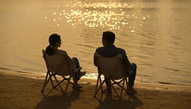 Couple relaxing on lakeshore chairs at golden hour sunset with sparkling water reflections