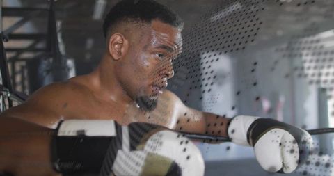 Determined Male Boxer Resting on Boxing Ring Ropes in Gym