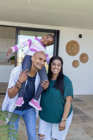 Joyful diverse family on sunlit terrace as father carries daughter on shoulders at home