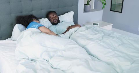 Couple sleeping peacefully in minimalist bedroom under light duvet and tufted headboard