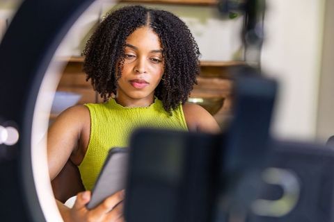 African woman creating content at home using tablet and ring light for online studio