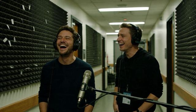 Laughing podcast hosts recording in acoustic studio corridor with microphone and headsets