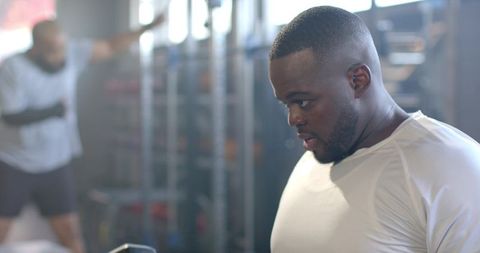 African American Trainer Spotting Trainee Lifting Dumbbell in Gym Strength Focus Coaching