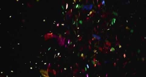 Multicolored confetti tumbling and shimmering with gold star sequins against dark backdrop