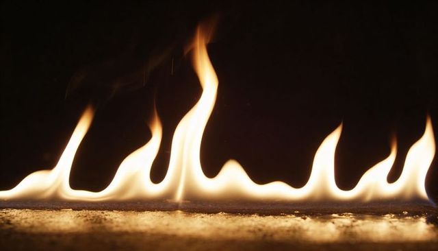 Low pale yellow flames dancing on reflective surface with amber glow and embers