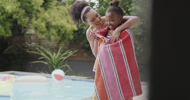 Mother drying her young daughter with towel near swimming pool. Both are smiling and enjoying summer outdoors. Suitable for depicting family bonding, summer activities, motherhood, parenting, happiness, and leisure time themes.